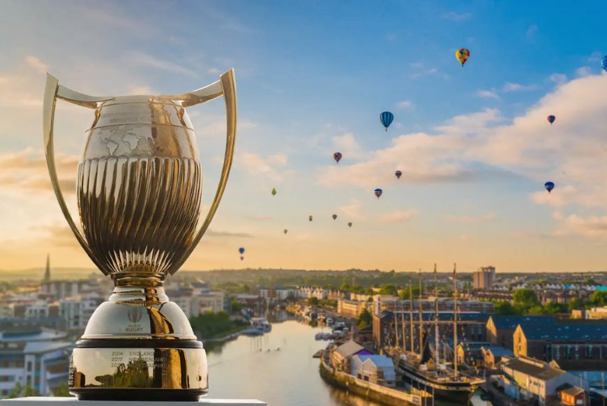 A trophy on a ledge overlooking a river with hot air balloons flying over a city